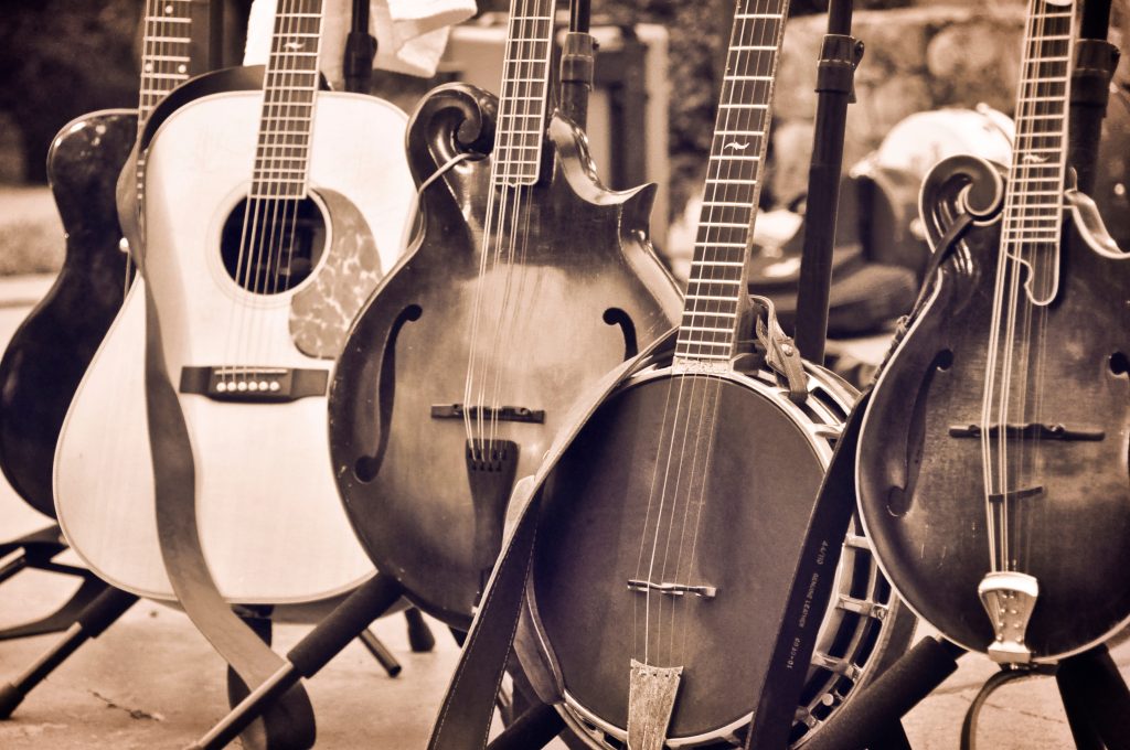 Image of acoustic folk instruments, including a guitar, banjo, and mandolin on instrument stands.