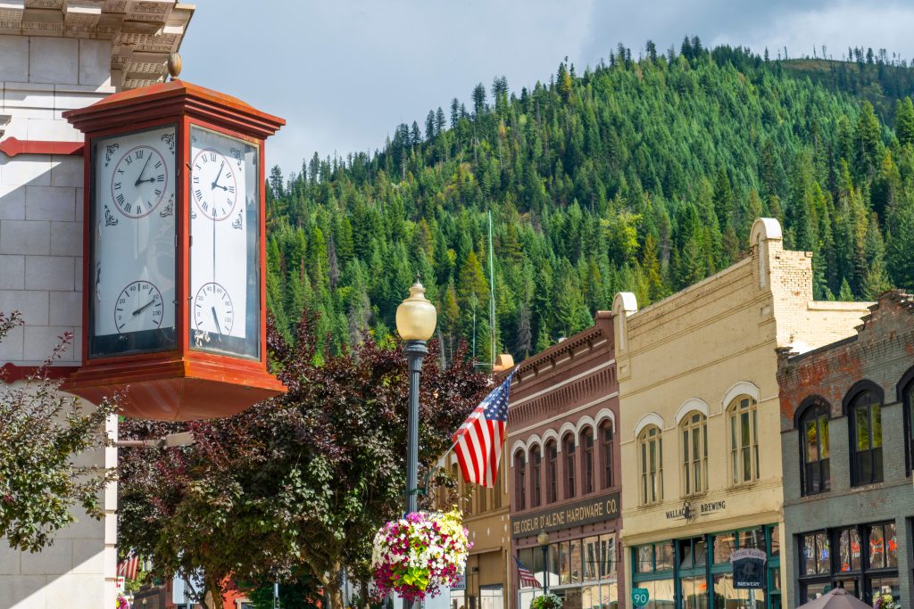 Picturesque downtown Wallace, Idaho, featuring the old train depot clock, historic building, a hanging floral basket, and an American flag.
